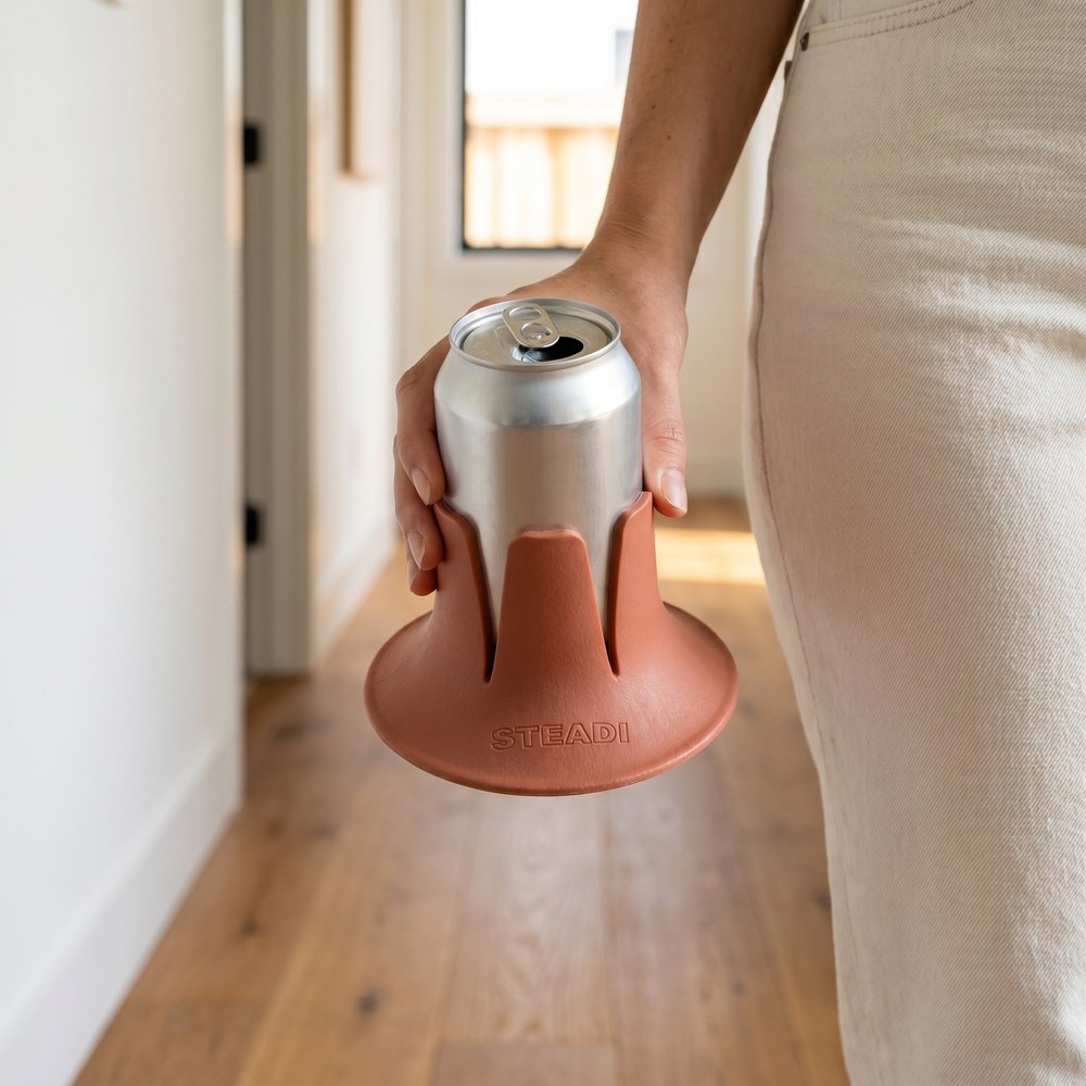 A hand carrying a can seated in a terracotta Steadi, holding it by the flared base.